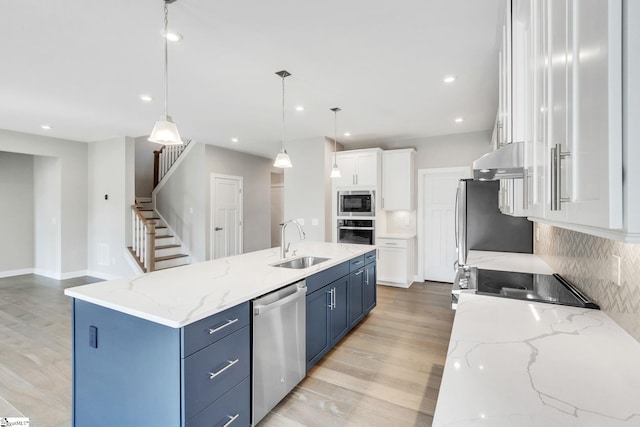 kitchen featuring decorative light fixtures, blue cabinetry, a kitchen island with sink, stainless steel appliances, and white cabinets