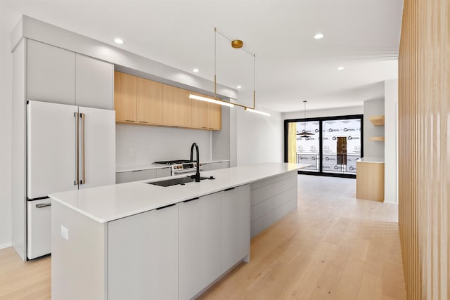 kitchen featuring light wood-type flooring, sink, an island with sink, white cabinets, and decorative light fixtures