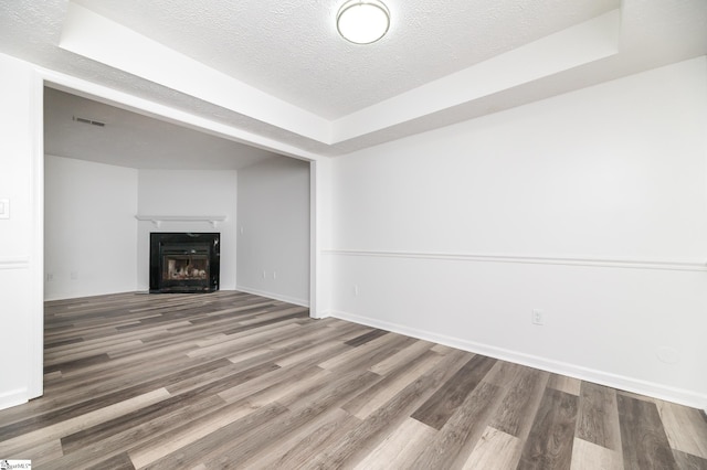 unfurnished living room featuring hardwood / wood-style flooring, a tray ceiling, and a textured ceiling