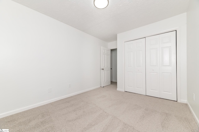 unfurnished bedroom featuring a textured ceiling, light carpet, and a closet