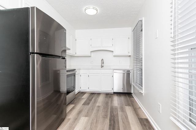 kitchen with sink, a textured ceiling, light hardwood / wood-style flooring, white cabinetry, and appliances with stainless steel finishes