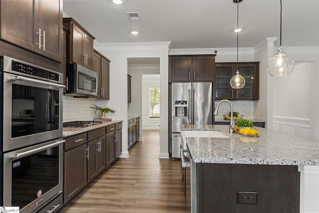 kitchen featuring dark brown cabinets, wood-type flooring, pendant lighting, a kitchen island with sink, and appliances with stainless steel finishes