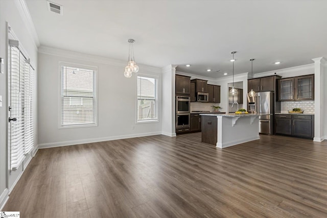 kitchen featuring an island with sink, appliances with stainless steel finishes, decorative light fixtures, and a breakfast bar area