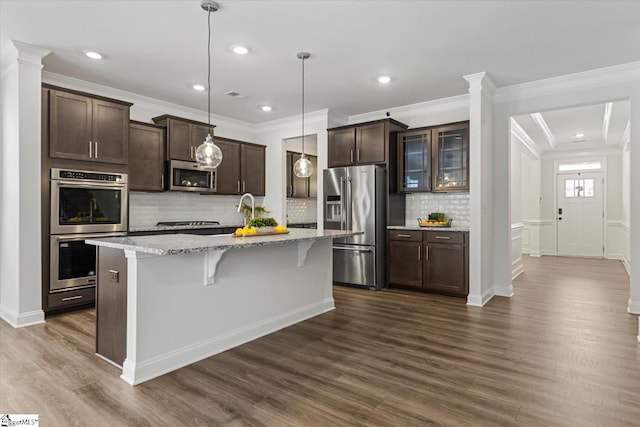 kitchen featuring stainless steel appliances, dark wood-type flooring, hanging light fixtures, and a kitchen island with sink