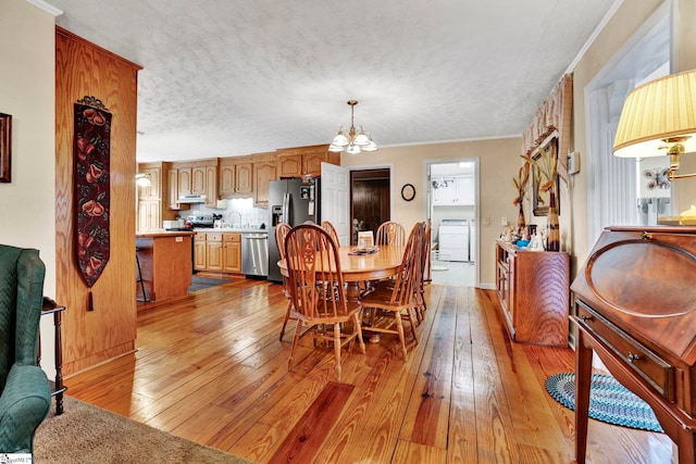 dining area with an inviting chandelier, light hardwood / wood-style flooring, washer / clothes dryer, a textured ceiling, and ornamental molding