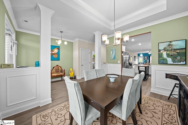 dining room featuring wood-type flooring, a notable chandelier, ornate columns, and ornamental molding