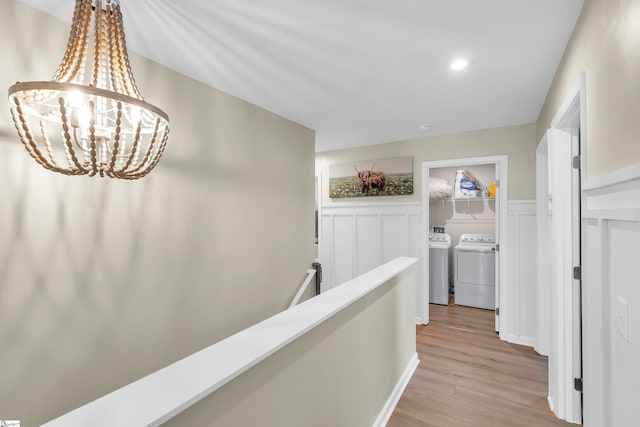 hallway featuring washing machine and clothes dryer, light wood-type flooring, and a notable chandelier