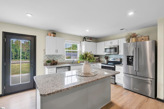 kitchen with appliances with stainless steel finishes, plenty of natural light, white cabinetry, and a center island