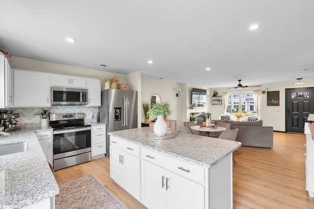 kitchen with appliances with stainless steel finishes, white cabinets, light wood-type flooring, a center island, and ceiling fan