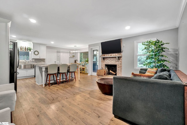 living room featuring a fireplace, light wood-type flooring, sink, and crown molding