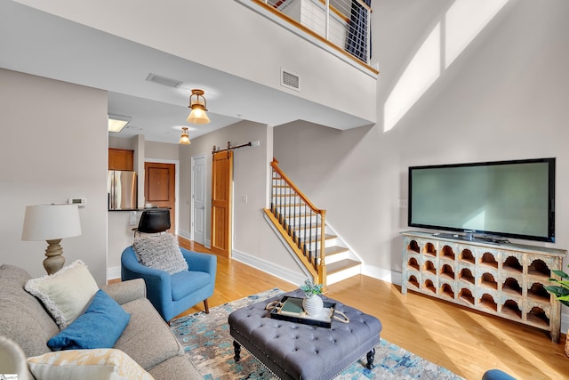 living room with a high ceiling, a barn door, and light hardwood / wood-style floors