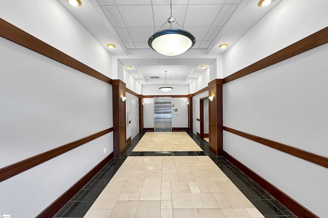 corridor featuring a paneled ceiling, a raised ceiling, and dark tile patterned floors