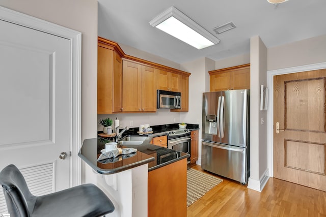 kitchen with sink, stainless steel appliances, kitchen peninsula, a breakfast bar area, and light wood-type flooring