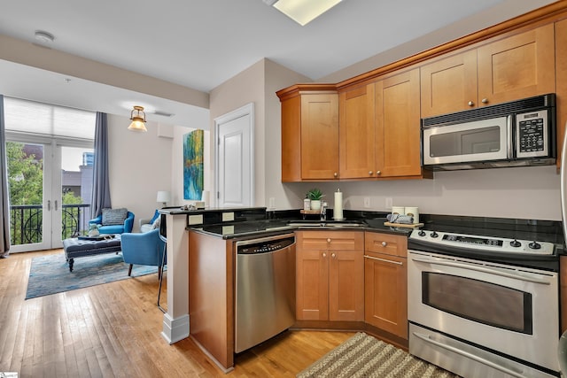 kitchen featuring sink, french doors, stainless steel appliances, dark stone counters, and light wood-type flooring