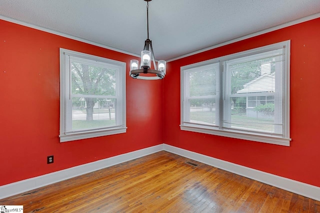 unfurnished dining area with a wealth of natural light, an inviting chandelier, hardwood / wood-style flooring, and crown molding