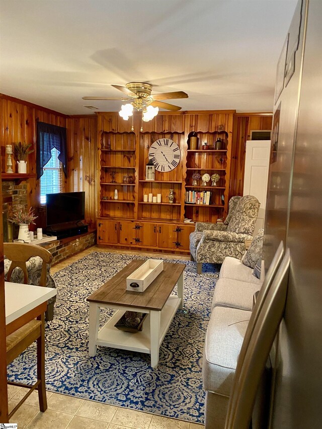 living room featuring ceiling fan, wooden walls, and light tile patterned floors