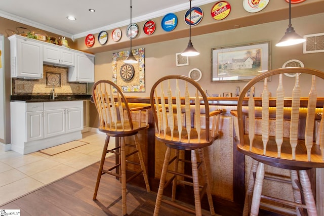 bar with ornamental molding, decorative light fixtures, white cabinetry, light wood-type flooring, and decorative backsplash