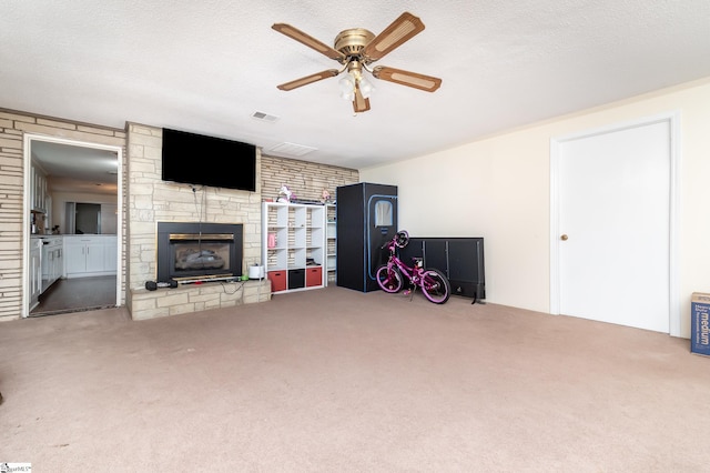 unfurnished living room with a textured ceiling, a stone fireplace, carpet flooring, and ceiling fan