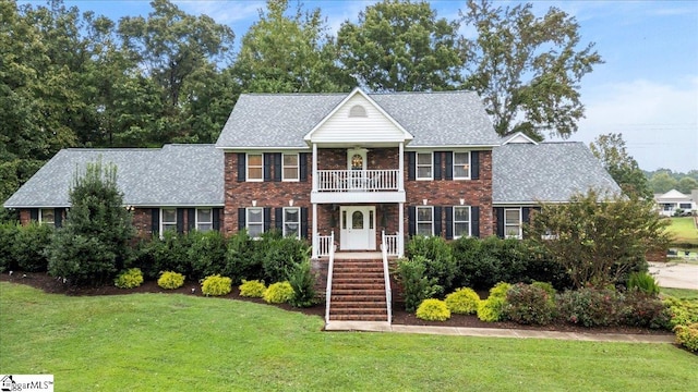 colonial house featuring a balcony and a front yard