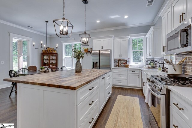 kitchen featuring butcher block counters, crown molding, a kitchen island, visible vents, and appliances with stainless steel finishes