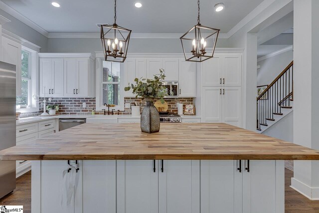 kitchen with butcher block countertops, white cabinets, an inviting chandelier, and ornamental molding