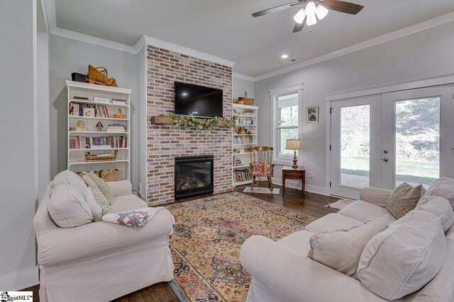 living room with a brick fireplace, crown molding, baseboards, a ceiling fan, and wood finished floors