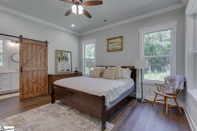 bedroom with ornamental molding, baseboards, a barn door, visible vents, and wood finished floors