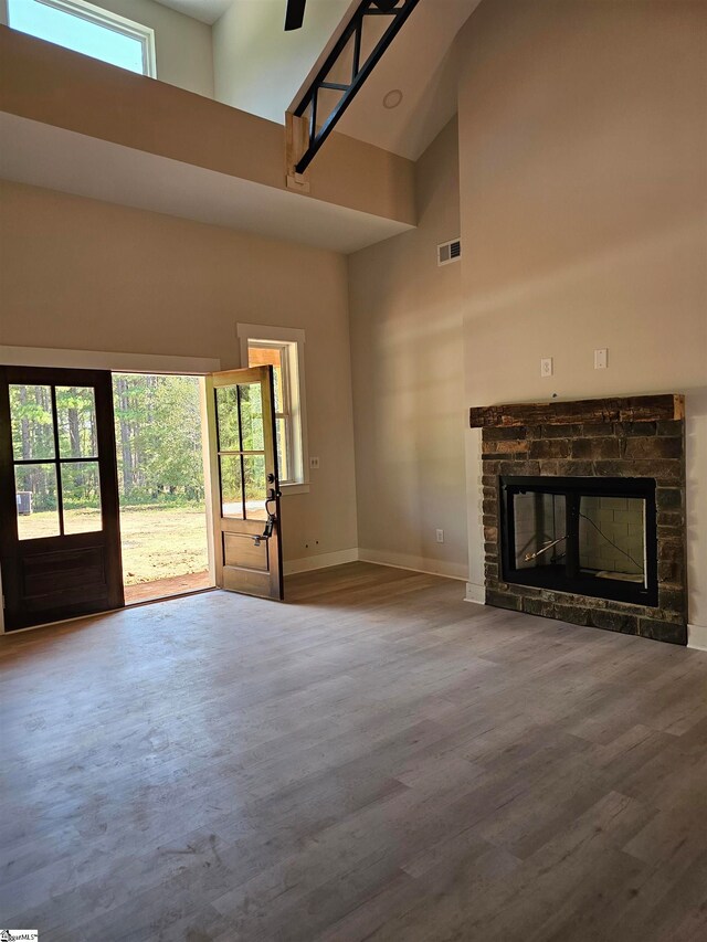 unfurnished living room featuring a stone fireplace, a high ceiling, and hardwood / wood-style floors