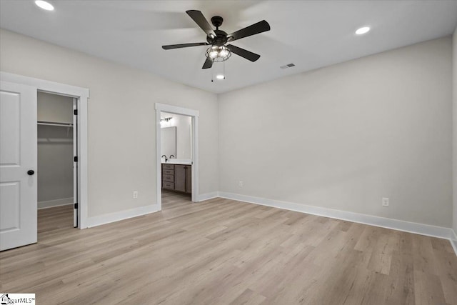 unfurnished bedroom featuring connected bathroom, a closet, a spacious closet, light hardwood / wood-style floors, and ceiling fan