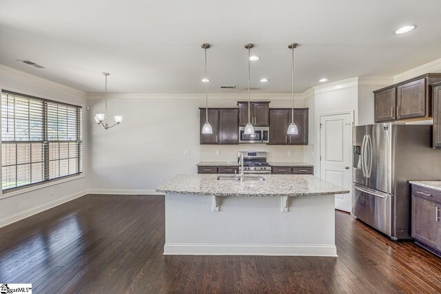 kitchen featuring appliances with stainless steel finishes, an island with sink, light stone countertops, pendant lighting, and sink