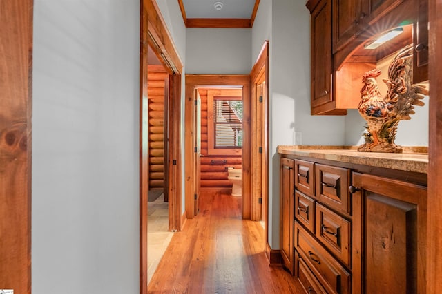 hall with light wood-type flooring, ornamental molding, and log walls