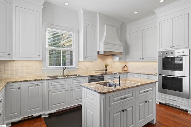 kitchen featuring white cabinets, stainless steel double oven, a kitchen island with sink, and sink