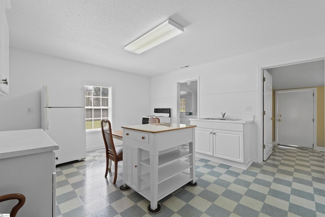 kitchen with white cabinets, sink, a textured ceiling, washer / dryer, and white fridge