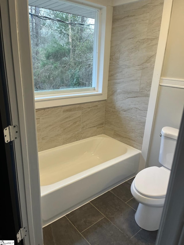 bathroom with toilet, a tub to relax in, tile walls, and tile patterned flooring