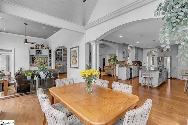 dining room with vaulted ceiling, ornate columns, light wood-type flooring, crown molding, and ceiling fan