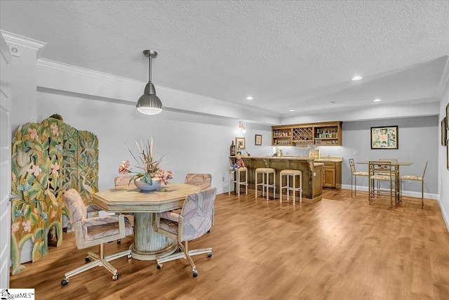 dining space with light wood-type flooring, crown molding, a textured ceiling, and bar area