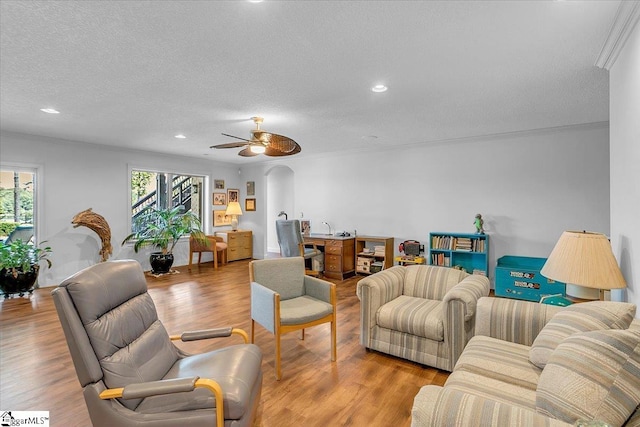 living room with ceiling fan, a textured ceiling, light wood-type flooring, and crown molding