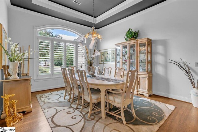 dining area with light hardwood / wood-style flooring, crown molding, a tray ceiling, and a chandelier