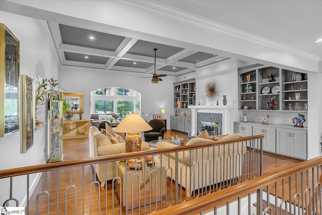 living room with light hardwood / wood-style floors, beamed ceiling, a tiled fireplace, coffered ceiling, and ceiling fan