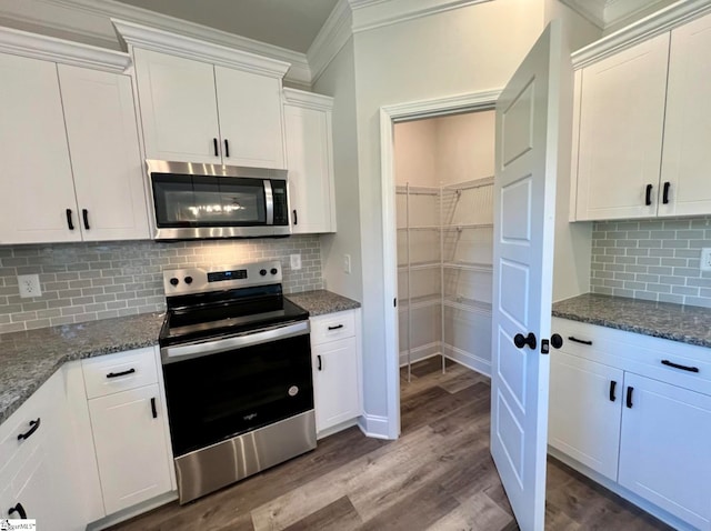 kitchen with white cabinets, ornamental molding, wood-type flooring, appliances with stainless steel finishes, and decorative backsplash