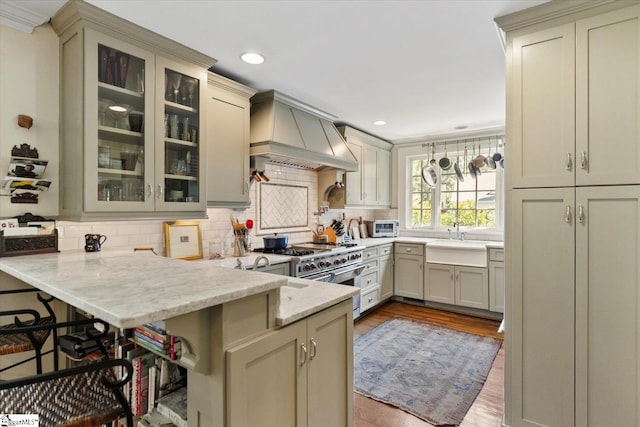 kitchen featuring a breakfast bar area, kitchen peninsula, decorative light fixtures, light stone countertops, and premium range hood