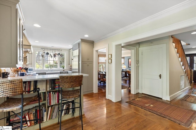 kitchen with a kitchen bar, ornamental molding, dark hardwood / wood-style flooring, and pendant lighting