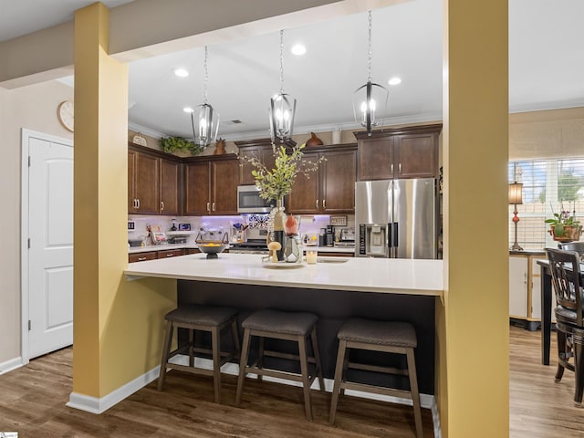 kitchen featuring appliances with stainless steel finishes, hanging light fixtures, a kitchen breakfast bar, wood-type flooring, and dark brown cabinets