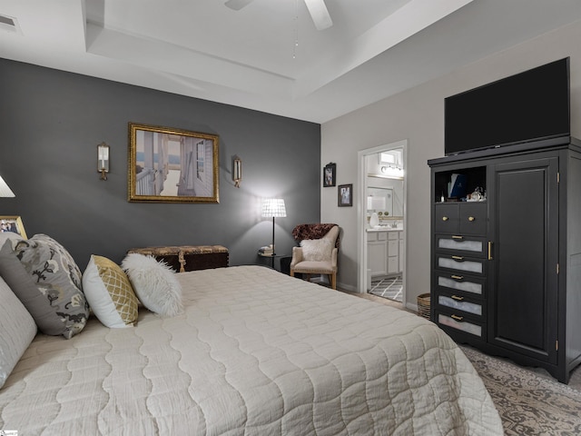 bedroom featuring a raised ceiling, ensuite bath, ceiling fan, and light colored carpet