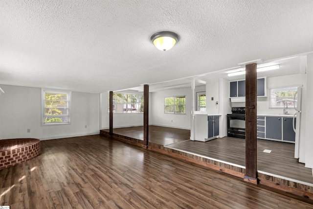 unfurnished living room featuring a textured ceiling, sink, dark wood-type flooring, and plenty of natural light