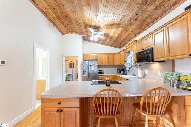 kitchen with light wood-type flooring, lofted ceiling, kitchen peninsula, black appliances, and ceiling fan