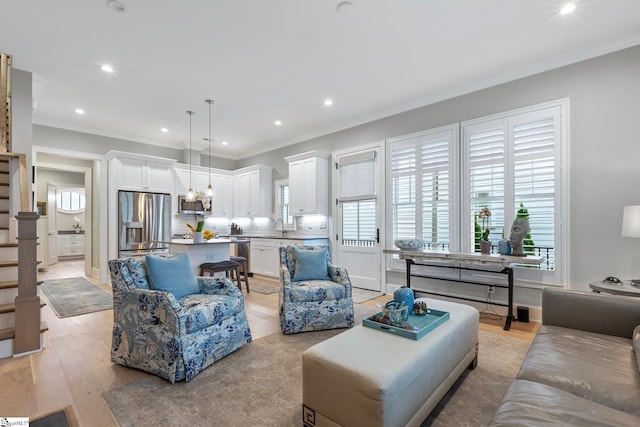 living room with ornamental molding, sink, and light hardwood / wood-style floors