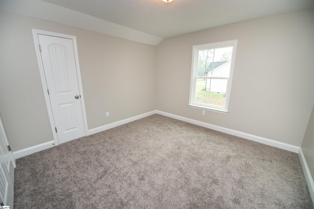 spare room with carpet, baseboards, and vaulted ceiling