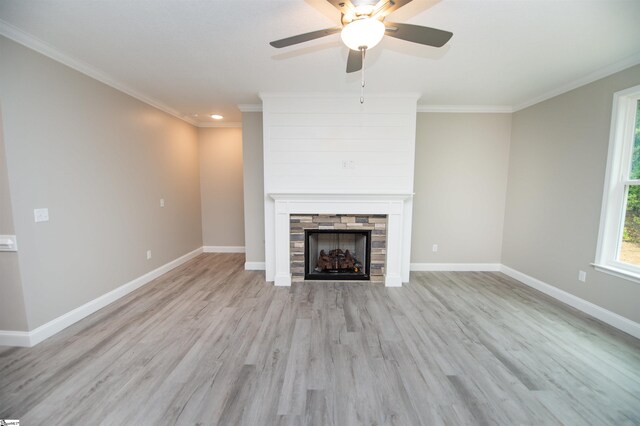 unfurnished living room with light wood-style flooring, a stone fireplace, baseboards, ornamental molding, and a ceiling fan