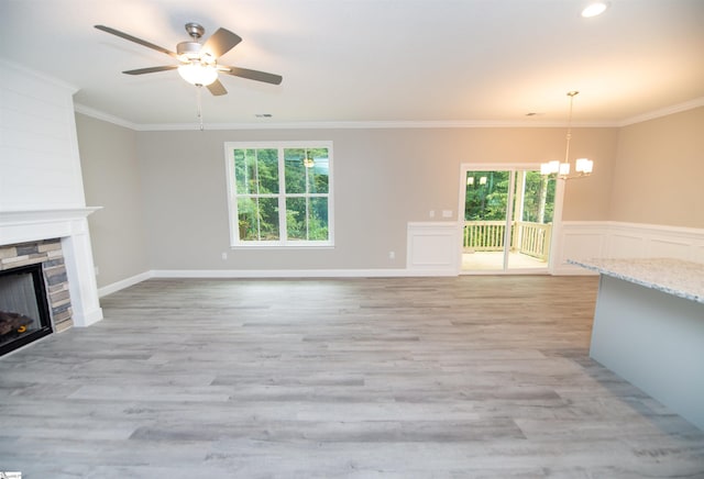 unfurnished living room featuring a chandelier, a stone fireplace, a ceiling fan, ornamental molding, and light wood-type flooring